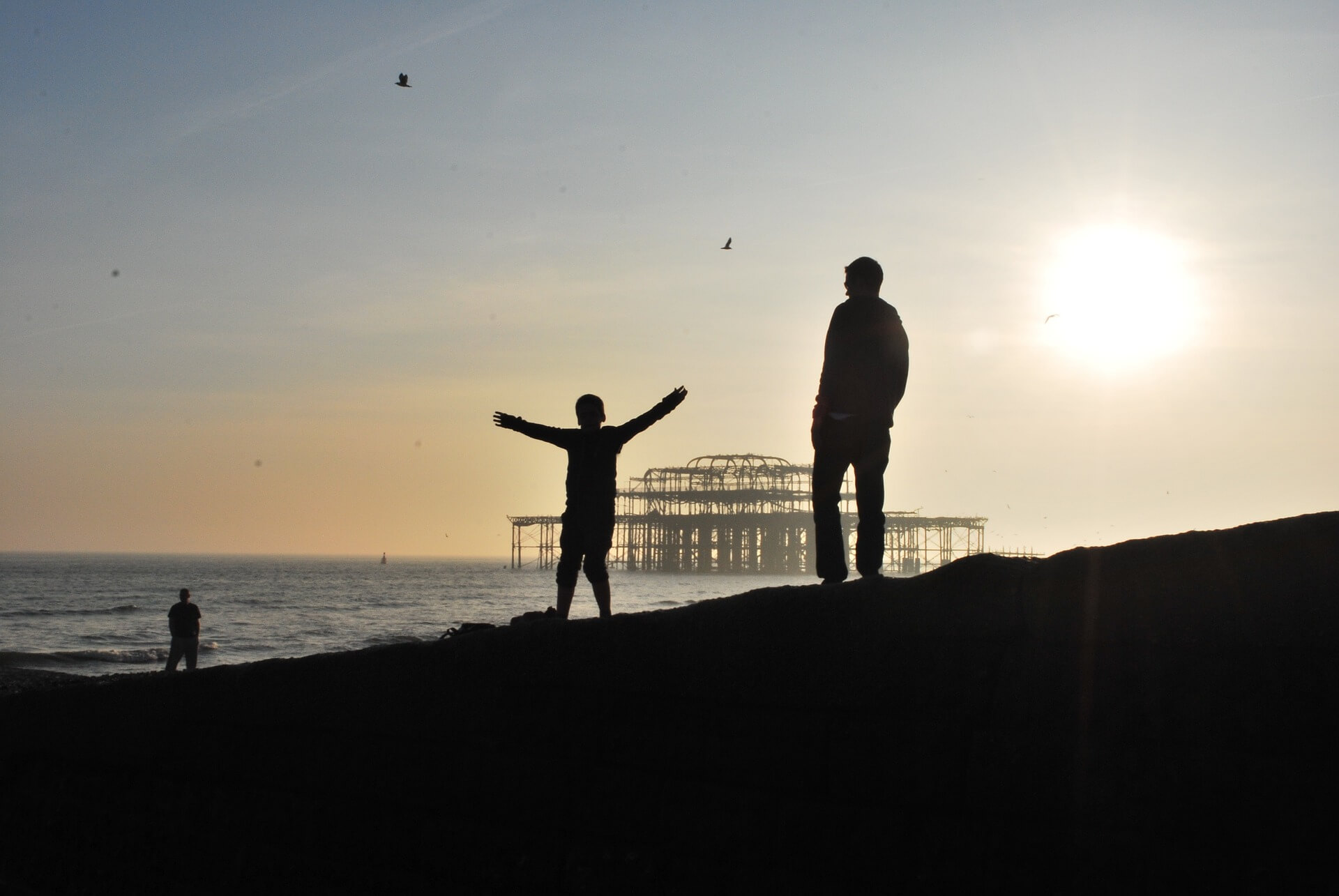 The silhouette of a father and son walking on a beach with a derelict pier in the background to help illustrate GBE's 'Community' section.